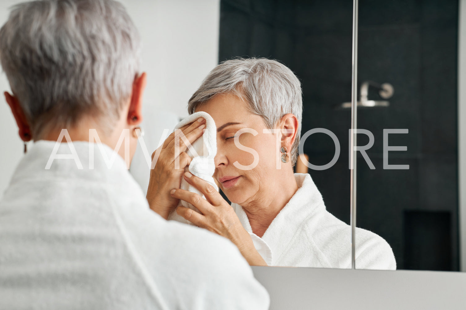 Mature woman standing in front of a mirror in bathroom doing a morning skincare routine	