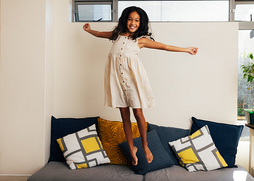 Happy girl jumping on couch in living room. Teenage girl having fun at home.