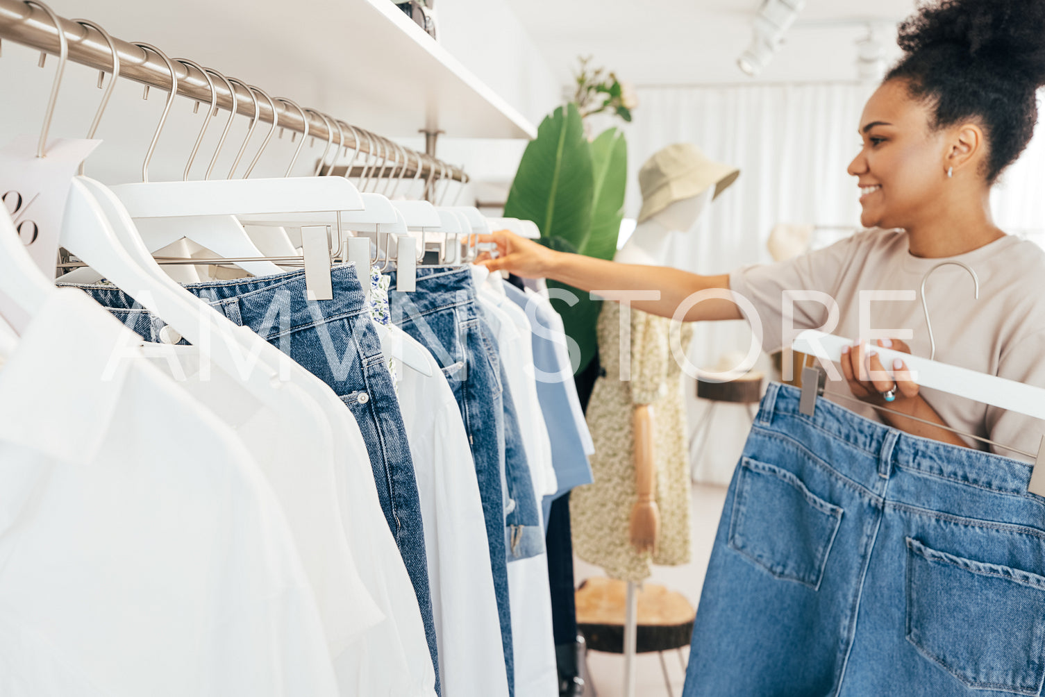 Side view of young saleswoman standing in a clothing store, hanging blue jeans on rail