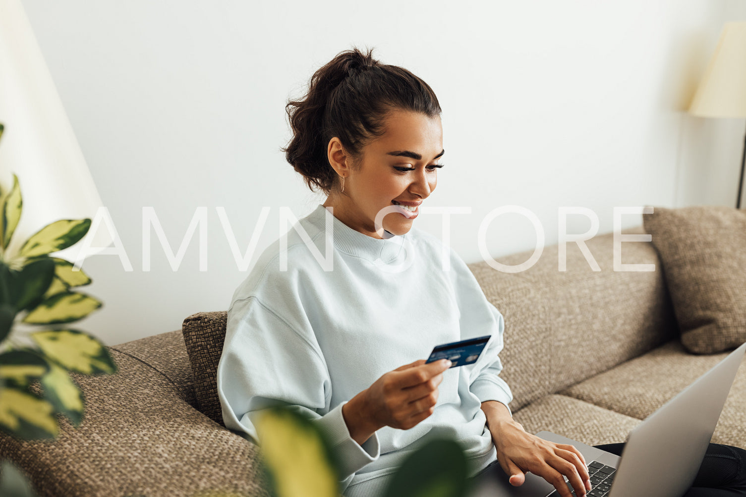 Smiling brunette woman doing online payment. Young female holding her credit card while typing on laptop.	