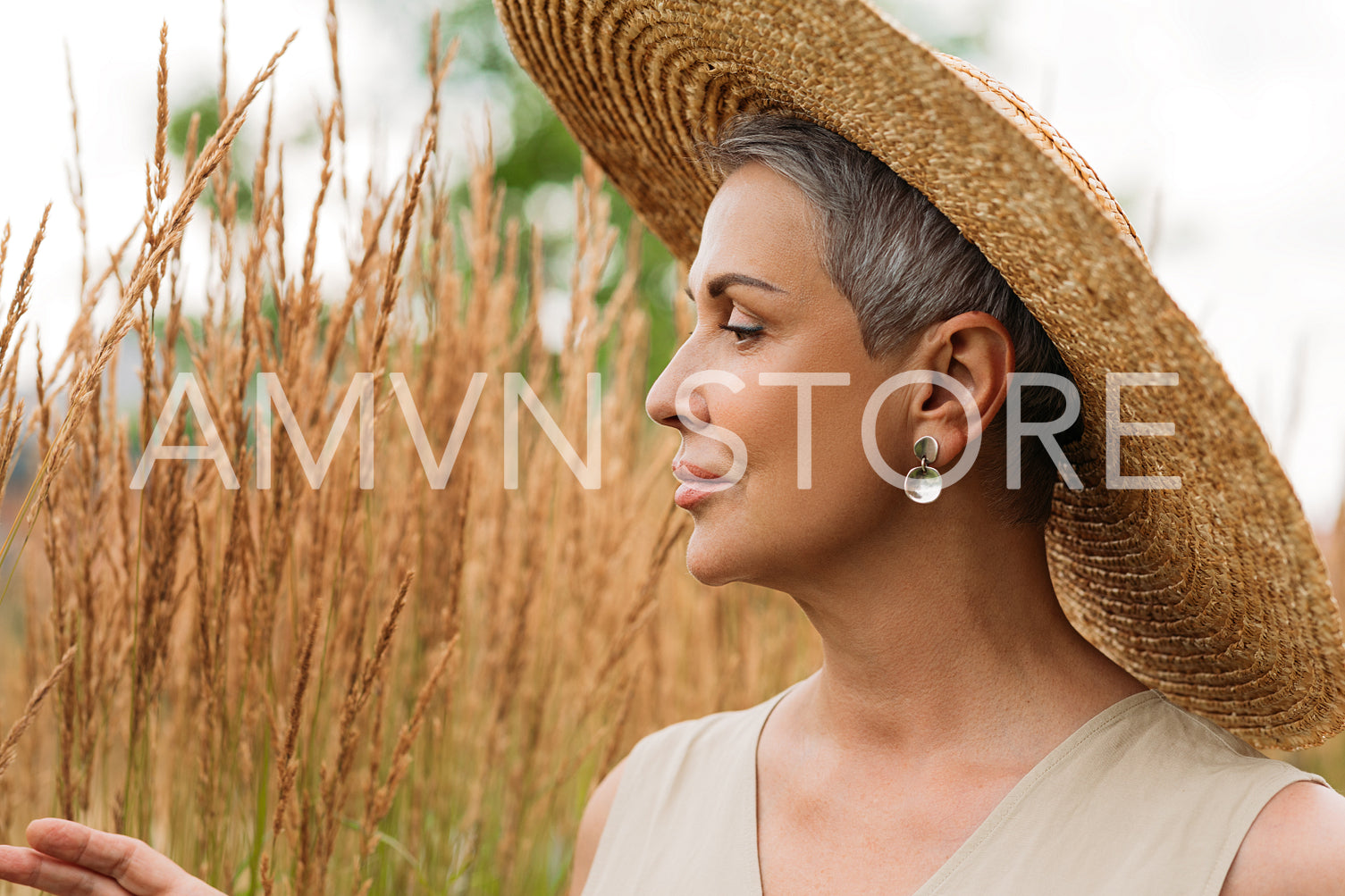 Side view of a senior woman in straw hat looking at wheat on a field