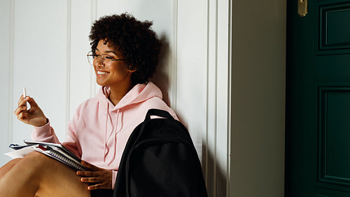 Smiling girl with books and digital tablet on her knees, looking away