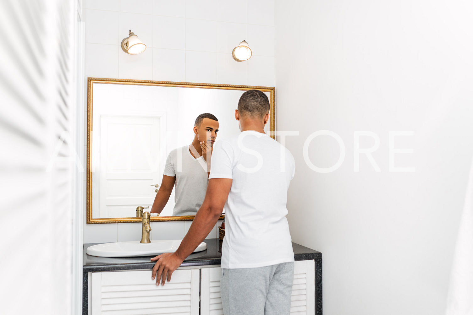 Rear view of handsome young man examining his face in the bathroom mirror	