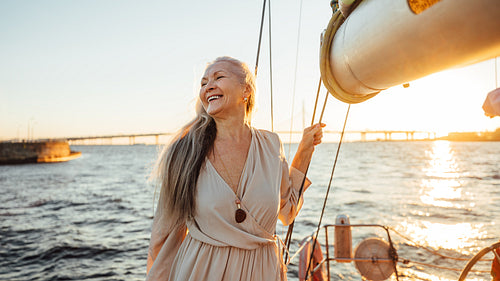 Happy mature woman standing on a yacht at sunset and looking away