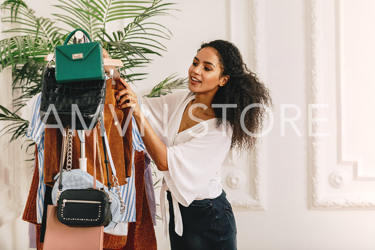 Young woman with curly hair looking at clothing on her rack	