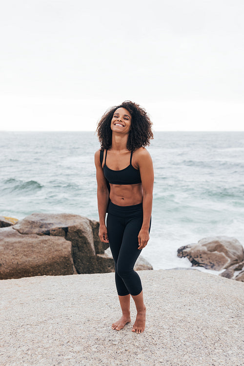 Full length of young woman standing by ocean relaxing after yoga exercises