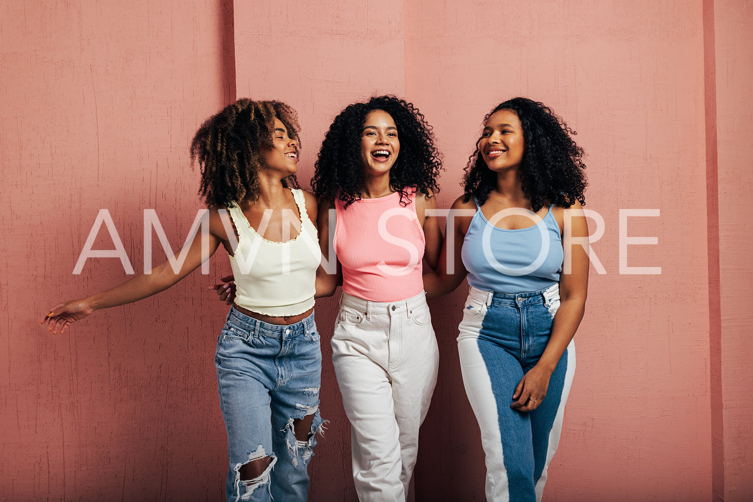 Three happy women with curly hair walk together. Young females having fun at a pink wall.