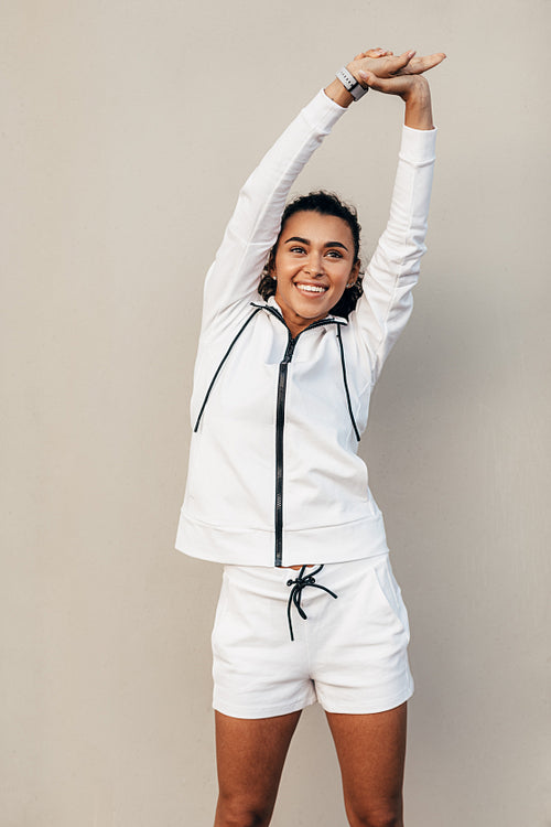 Smiling sportswoman doing stretching exercises at a wall