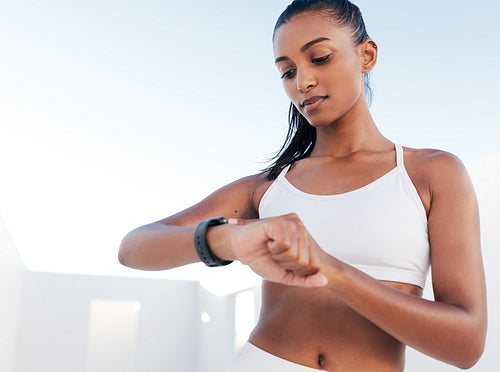 Slim female athlete looking at smartwatch. Woman in white fitness clothes standing outdoors checking her heart rate.