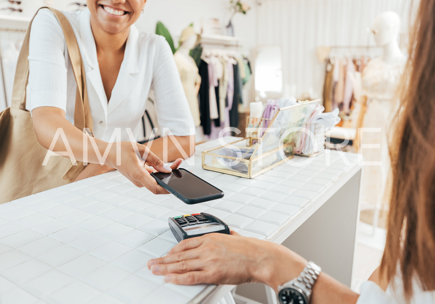 Cropped shot of a smiling young woman using smart phone to pay at counter