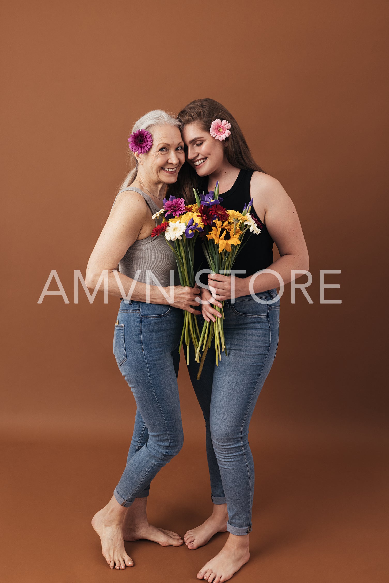 Two women with flowers posing in a studio a brown background