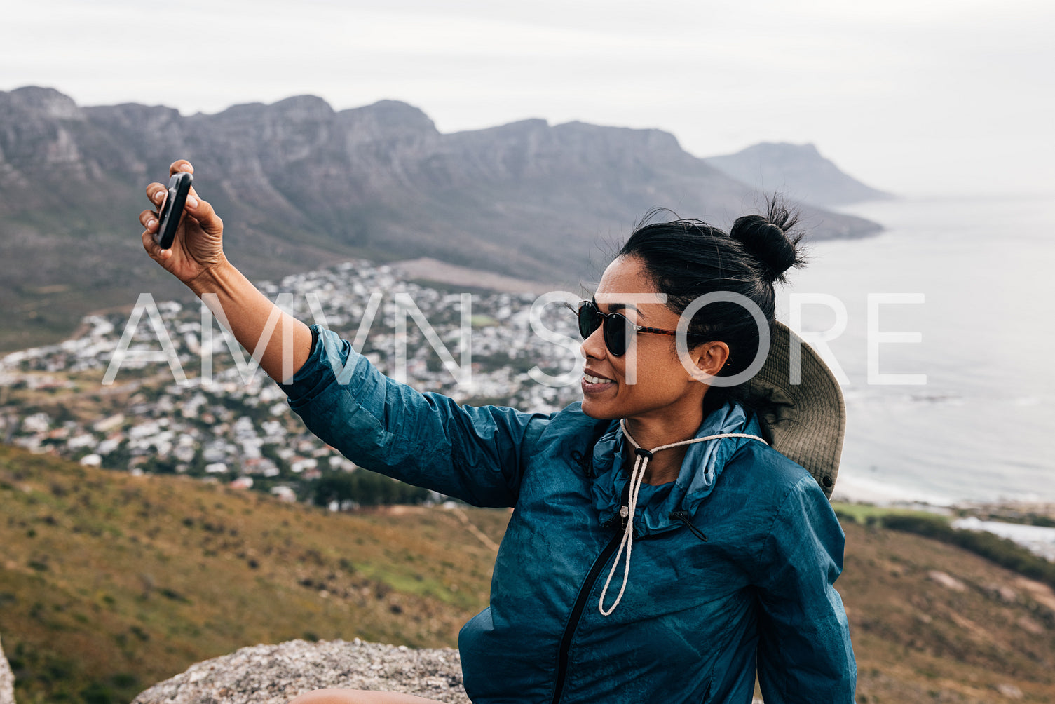 Young woman in sunglasses holding a smartphone and taking a selfie while taking a break during a mountain hike