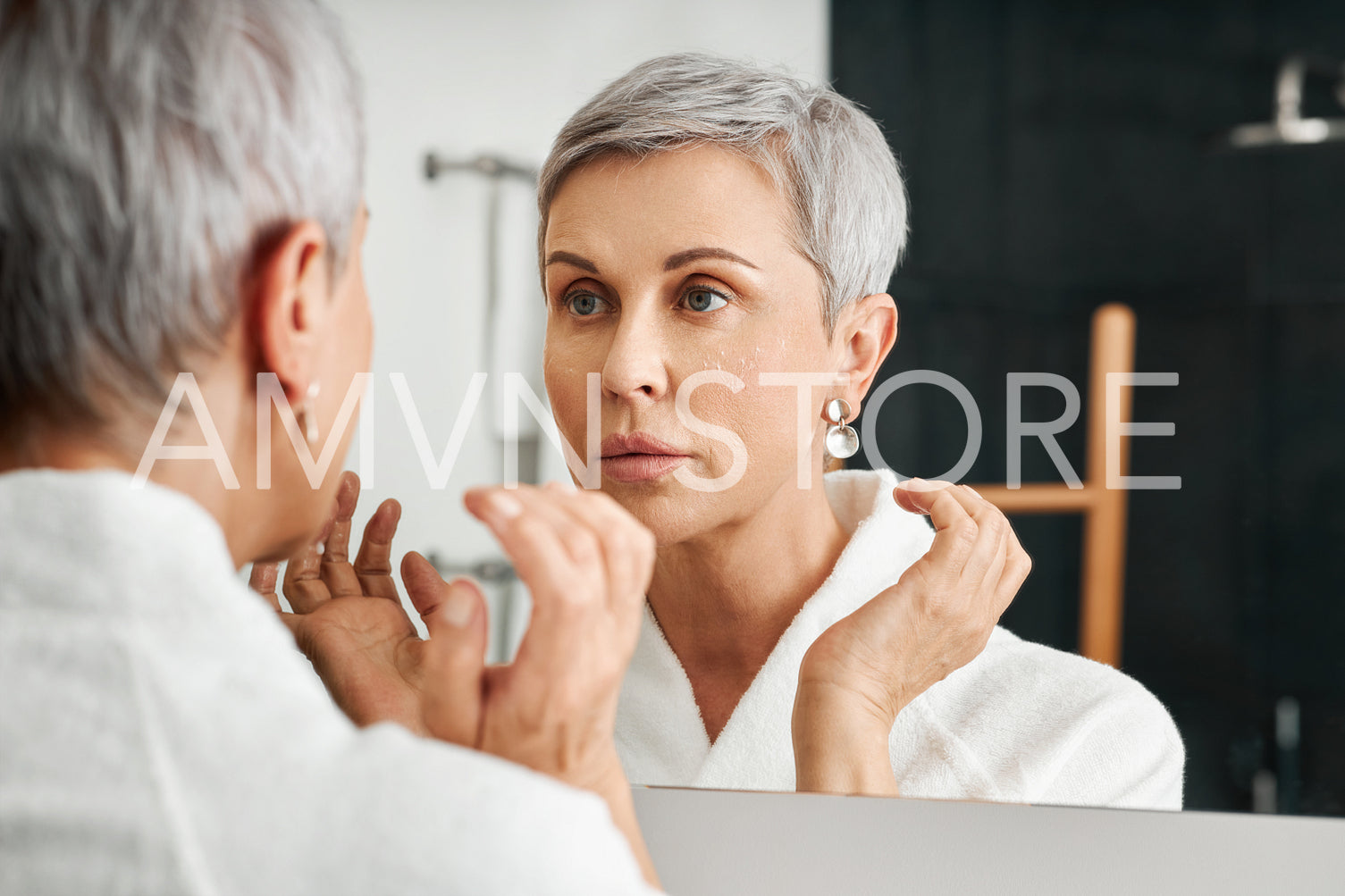 Senior woman with moisturizer on her face looking at mirror in bathroom	