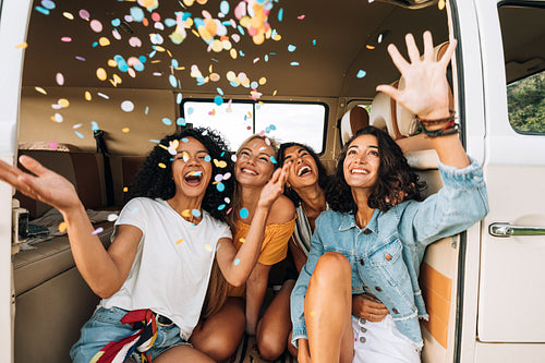 Women friends throwing confetti in the air while sitting in camper van