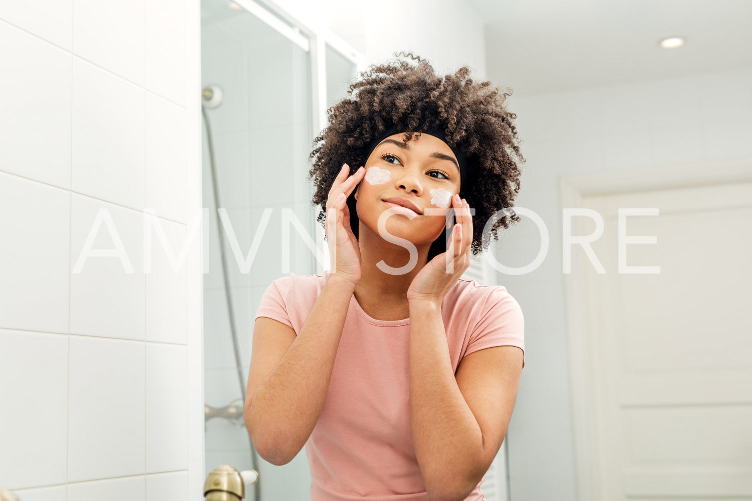 Young woman putting cosmetic cream on her face and looking into a mirror	