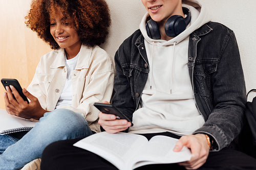 Cropped shot of two university students reading from smartphones while preparing exams