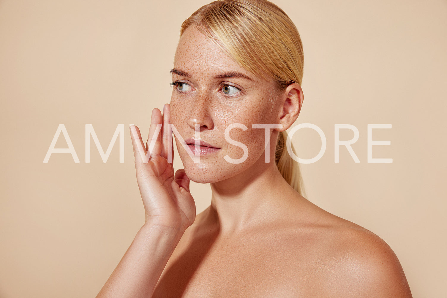 Studio shot of a young woman with freckles touching her face