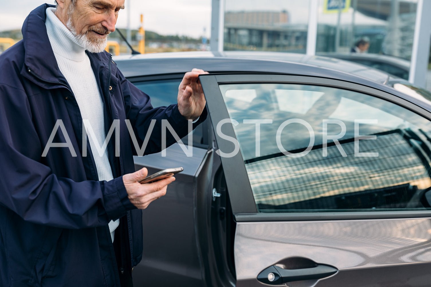 Mature man opening a door of his car. Bearded man looking on smartphone outdoors.	