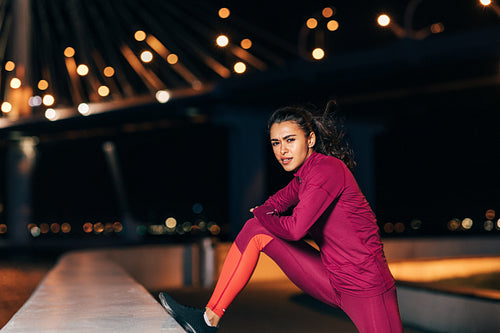 Woman stretching before an evening run. Young female jogger warming up legs at night.