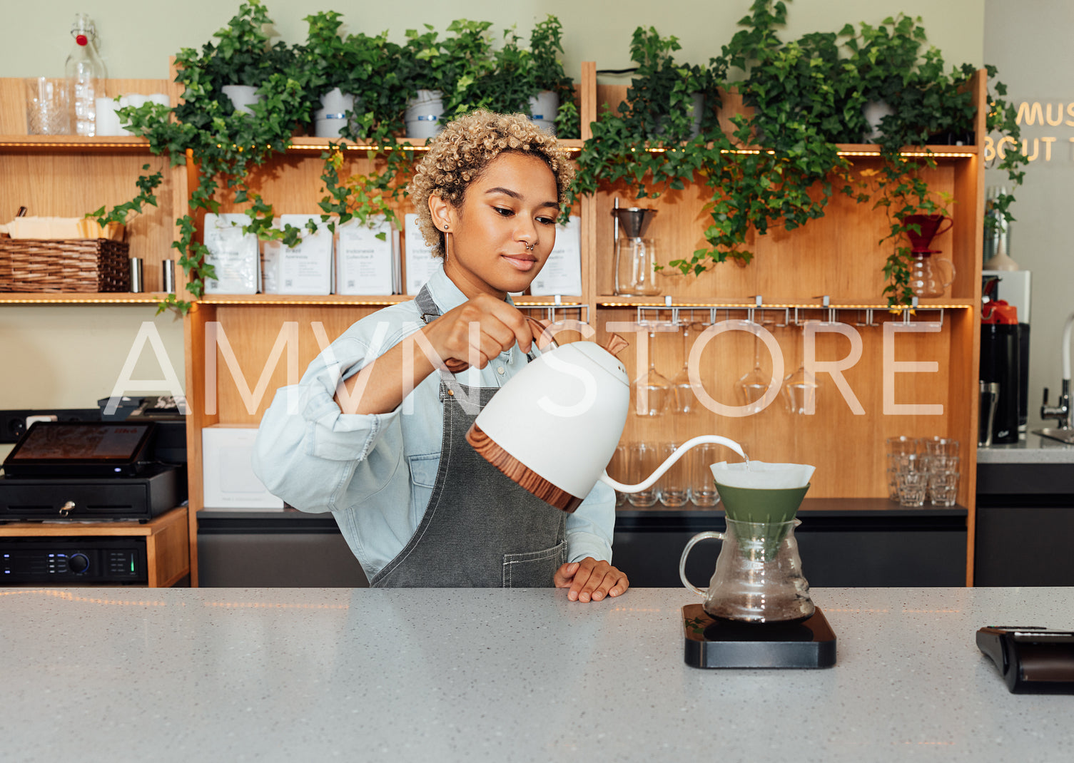 Young female barista with short hair preparing coffee with a filter at the counter