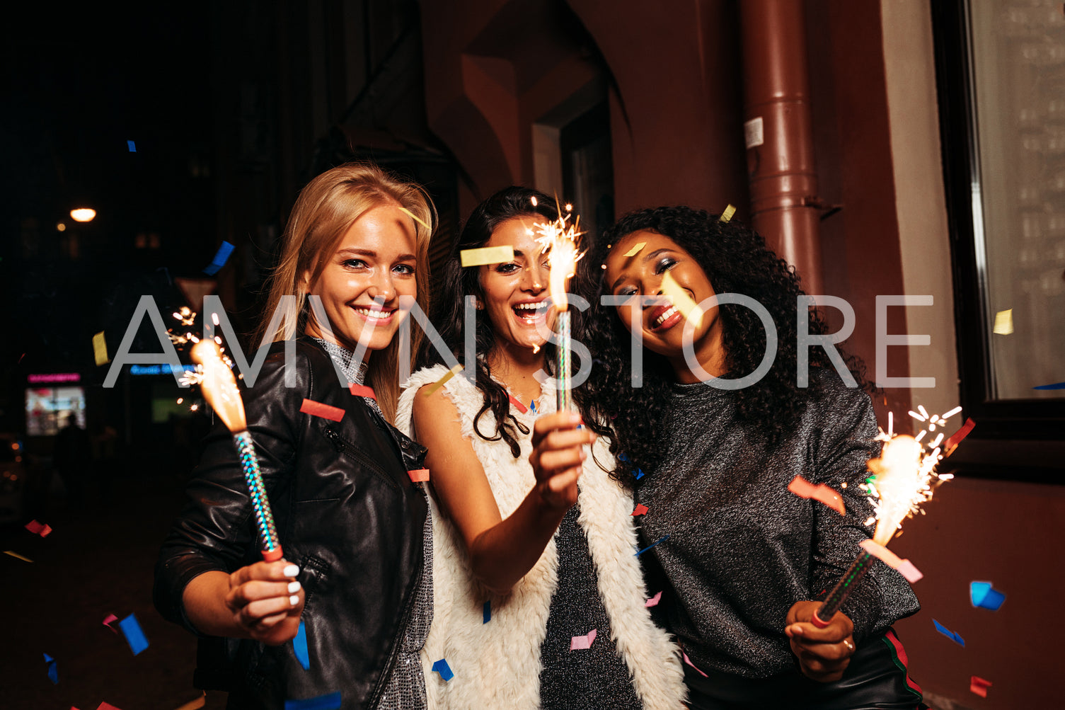 Three female friends holding sparklers on street	