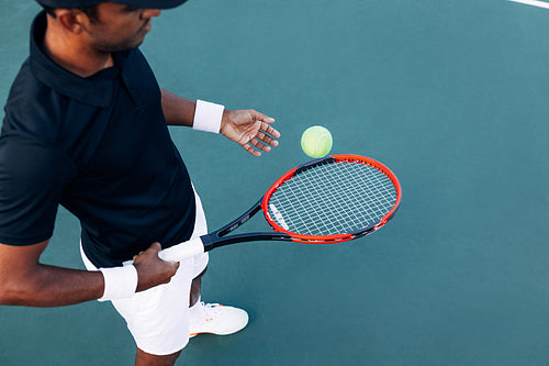 High angle of an unrecognizable tennis player bouncing a ball with a racket