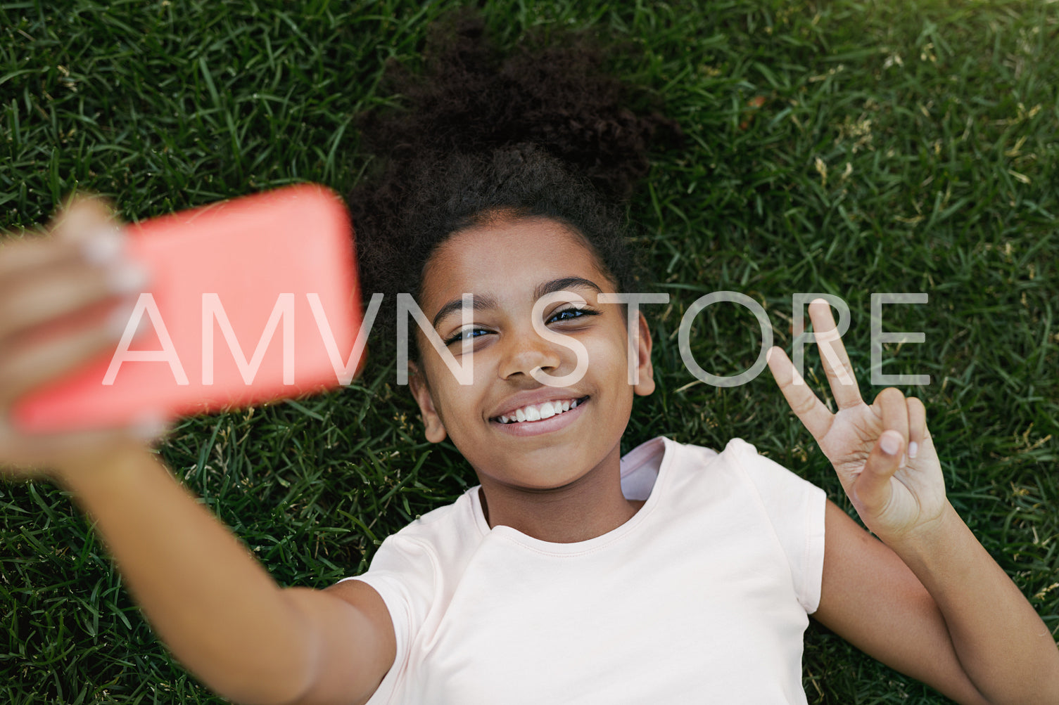 Smiling girl taking selfie on her smartphone, lying on grass in park	