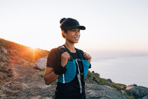 Portrait of smiling woman in hiking sportswear standing on the top of the mountain at sunset