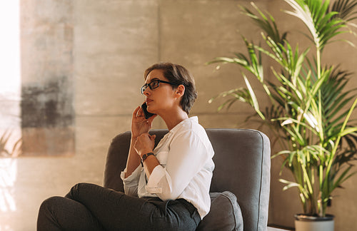 Side view of a middle-aged woman in formal wear sitting indoors and talking on a mobile phone