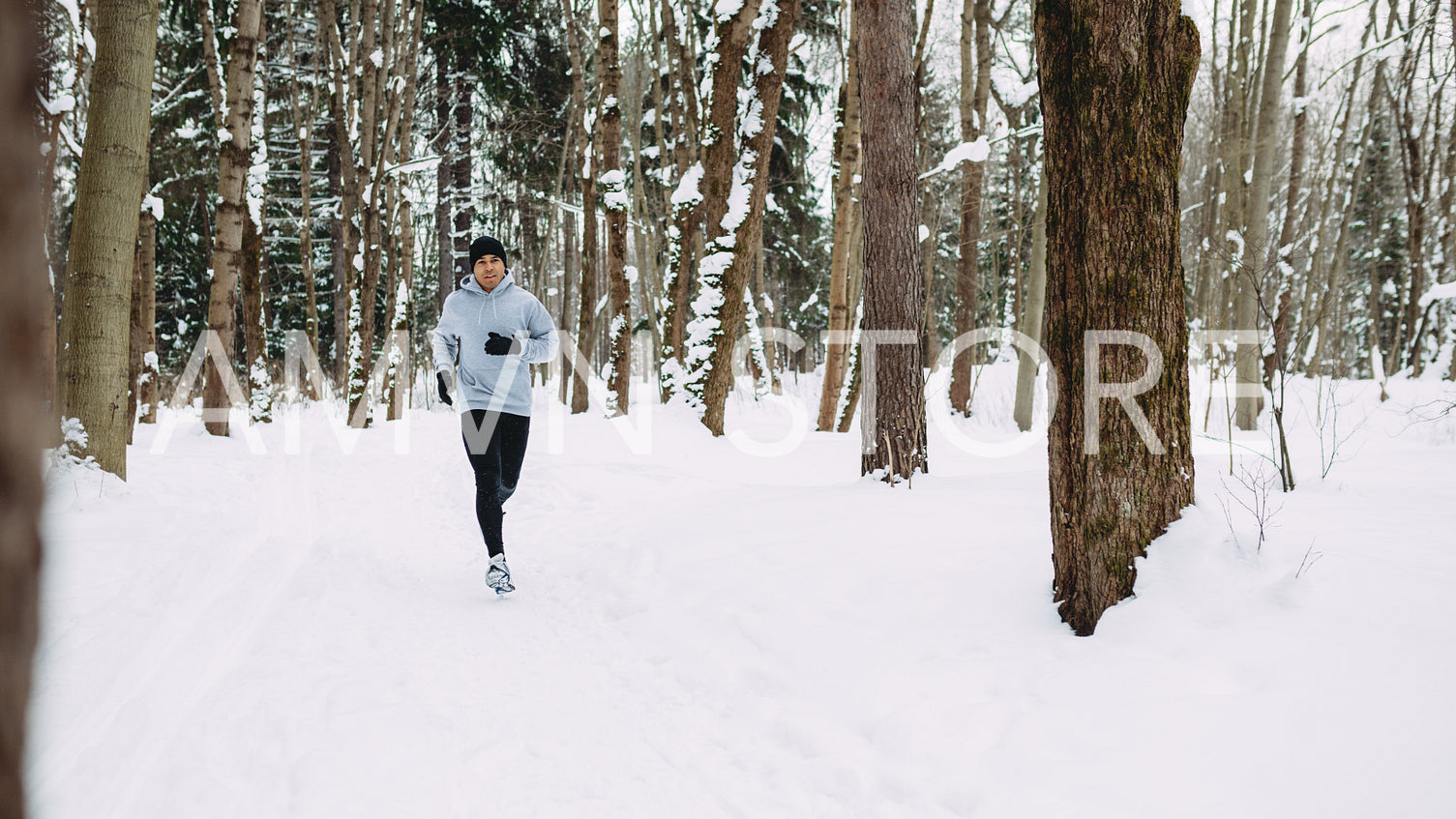 Young man exercising at winter, running through the forest	
