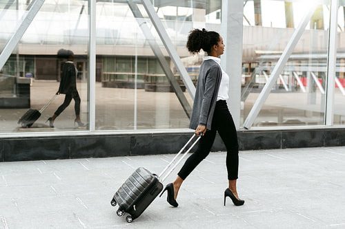 Travelling businesswoman walking with luggage at station, side view