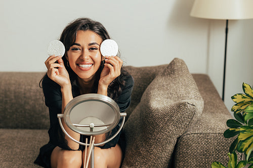 Happy woman with two sponges sitting on a couch and looking at camera