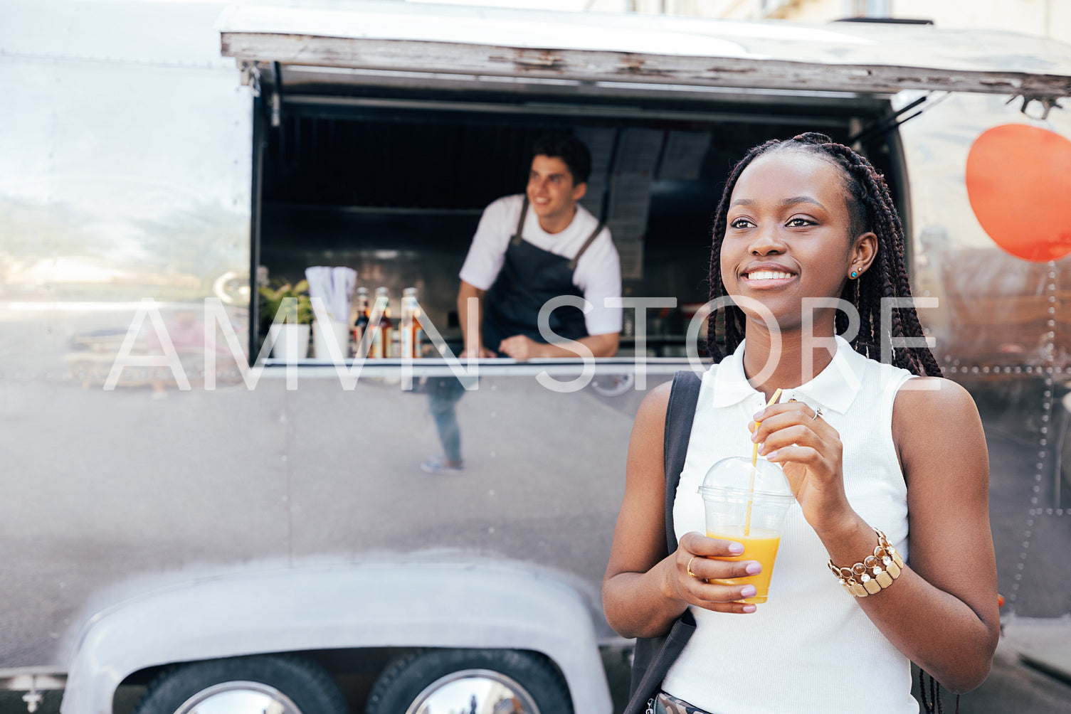 Young female with juice standing against a food truck. Girl with orange juice that she bought in a food truck.