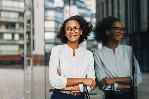 Smiling businesswoman standing outside a office building. Woman in formal wear looking away.