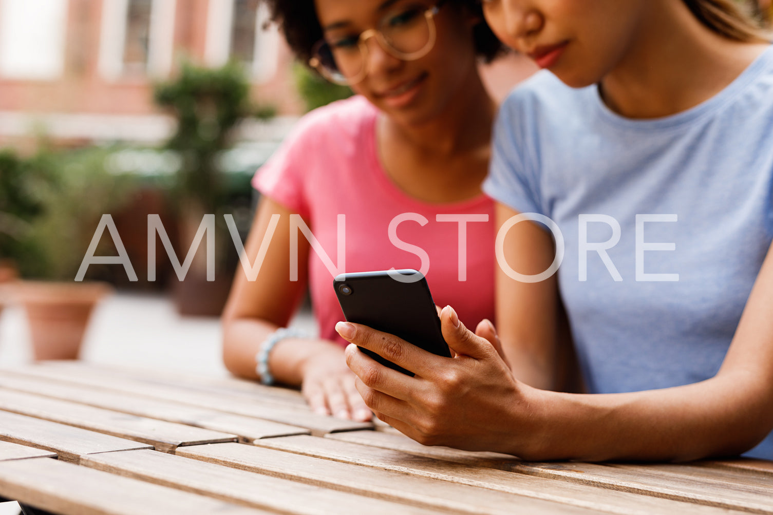 Croppped shot of two women sitting at restaurant and looking on mobile phone	