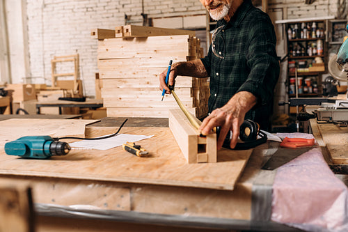 Unrecognizable senior carpenter measuring length of wooden plank in workshop