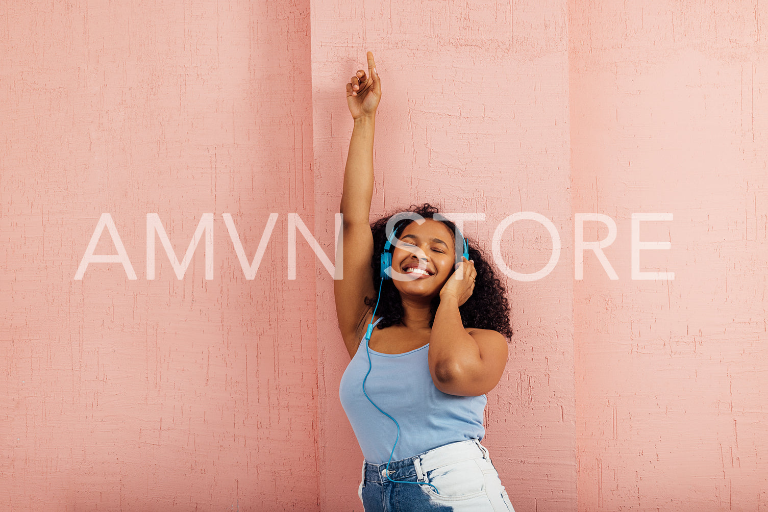 Happy woman wearing blue headphones leaning on a wall and smilin