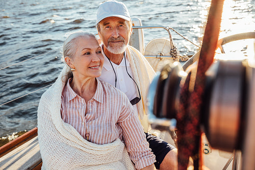 Mature couple sitting on yacht and wrapped in a white blanket