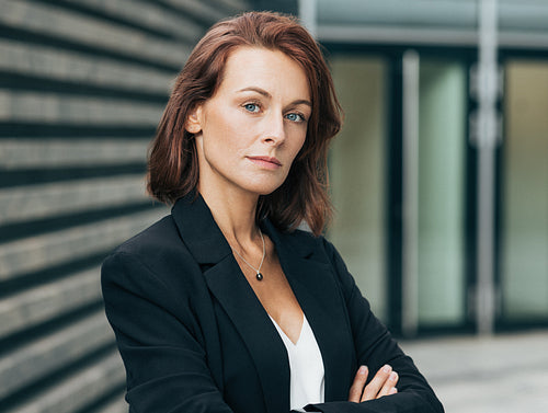 Portrait of a confident female with ginger hair standing with crossed arms looking straight to camera. Close-up portrait of a corporate person.