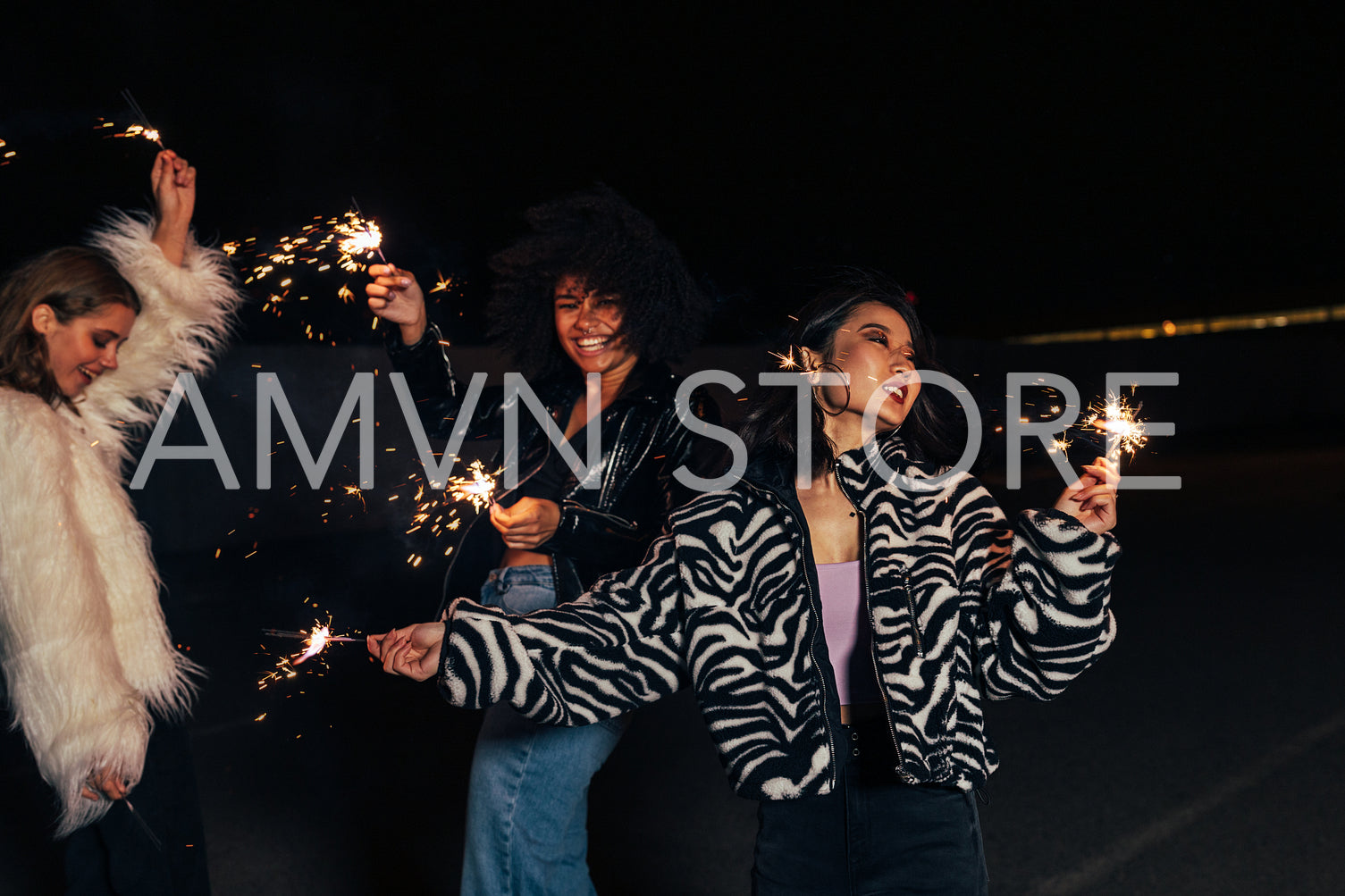 Laughing female girlfriends dancing outdoors with sparklers at night	