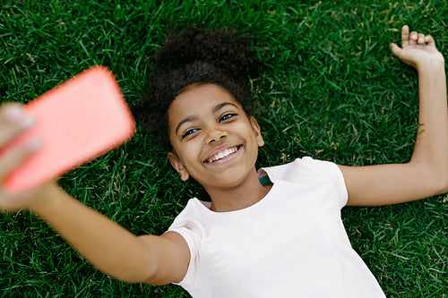 Smiling girl lying on a grass and taking selfie on mobile phone