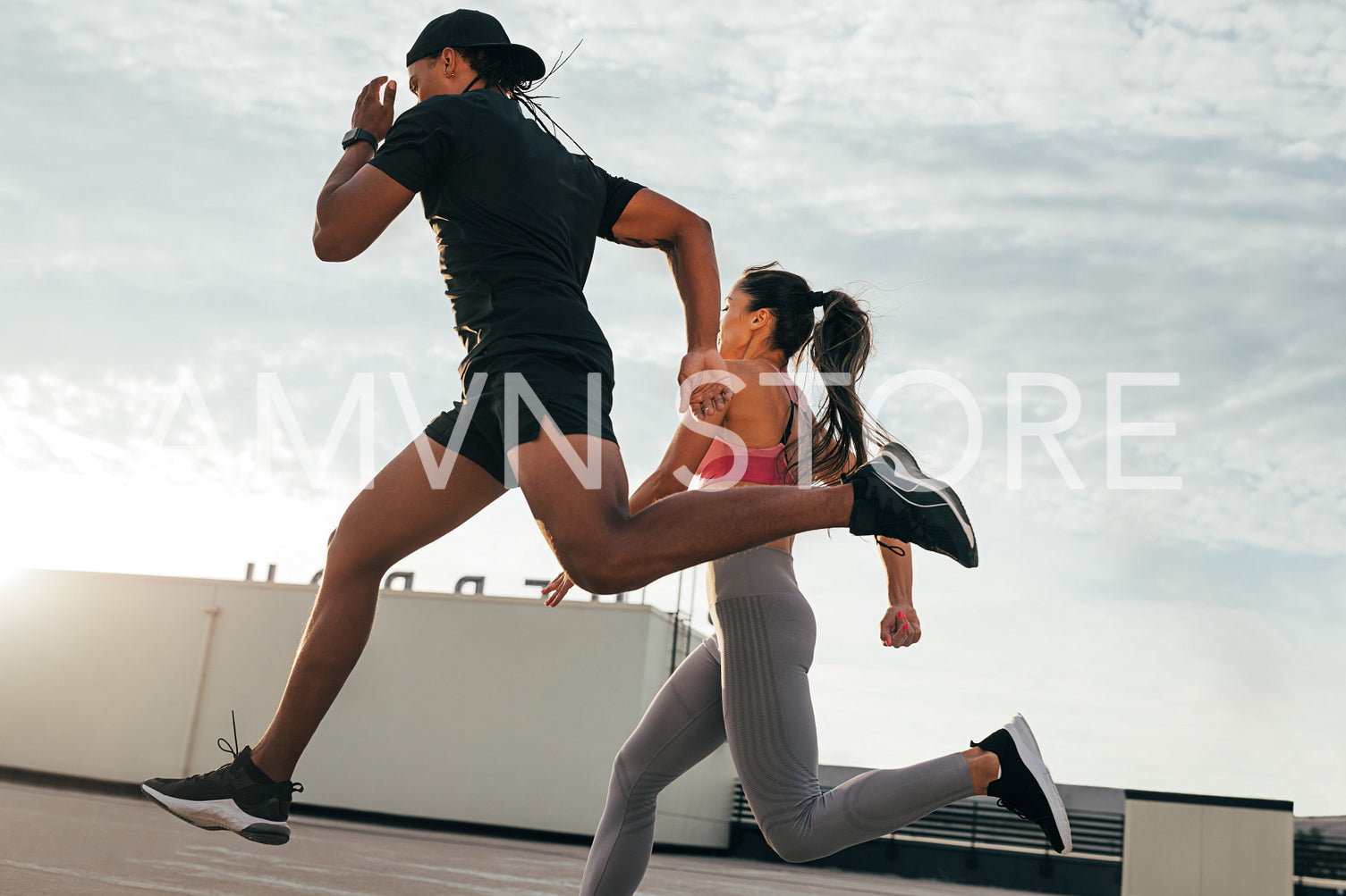 Fitness couple running and jumping on the roof. Athletes sprinting on the roof at sunset.