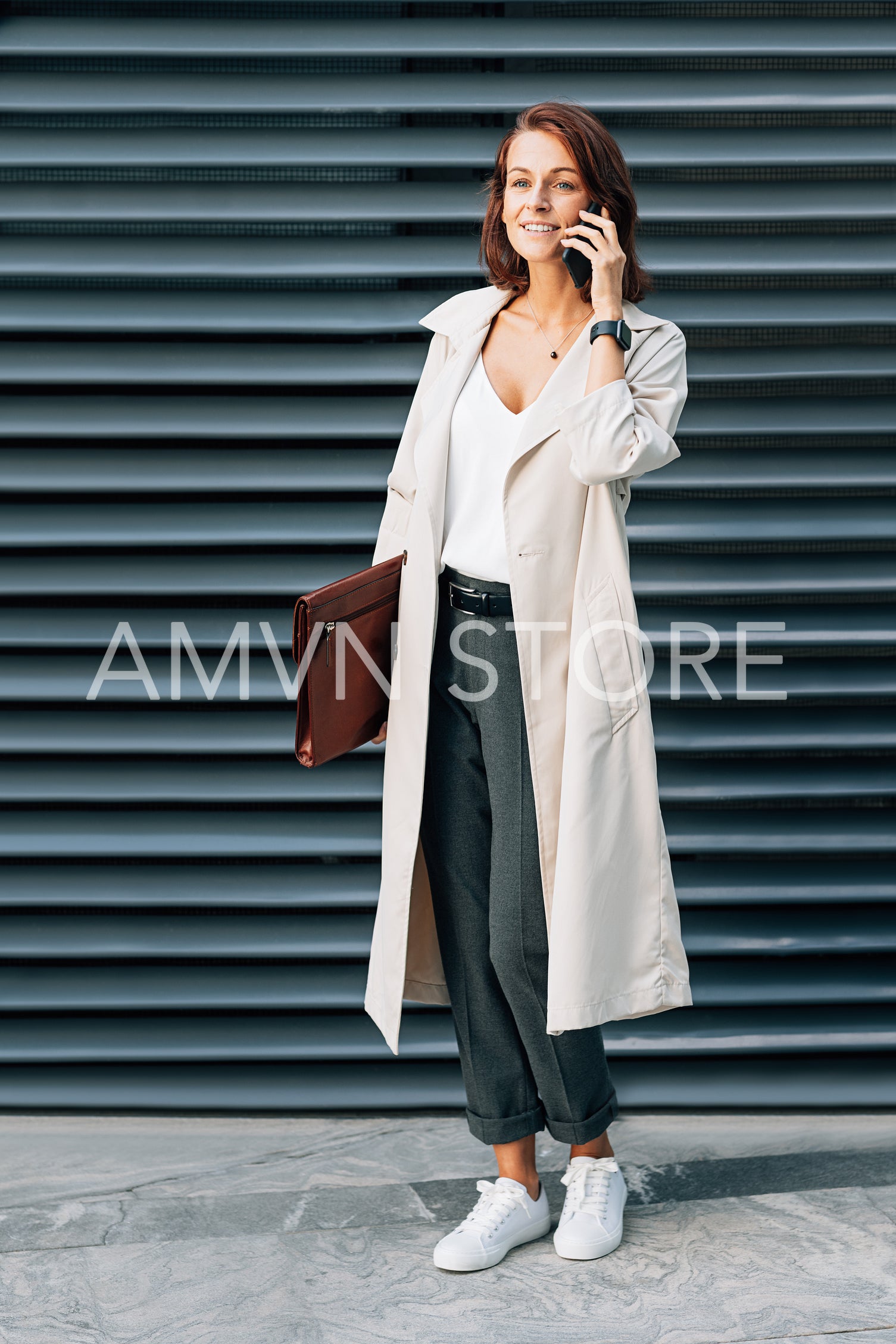 Full length of a stylish businesswoman with a folder talking on a mobile phone outdoors