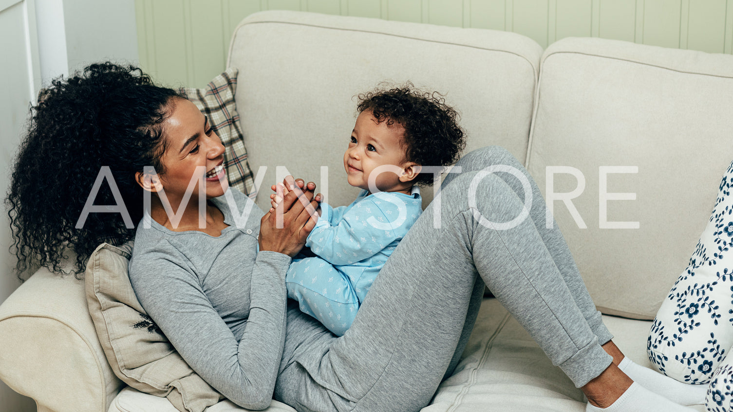 Mother playing with baby boy lying on sofa	