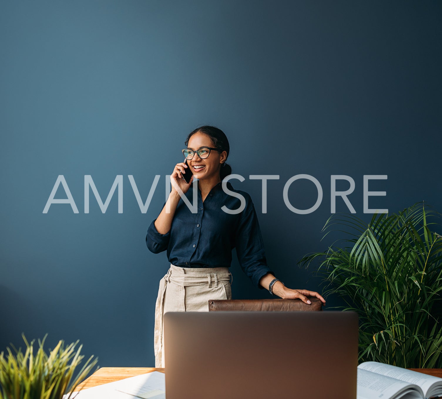 Smiling entrepreneur in formal wear talking on a cell phone while standing at a blue wall at home