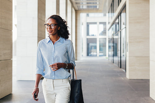 Female business professional walking outside an office building with bag on a hand