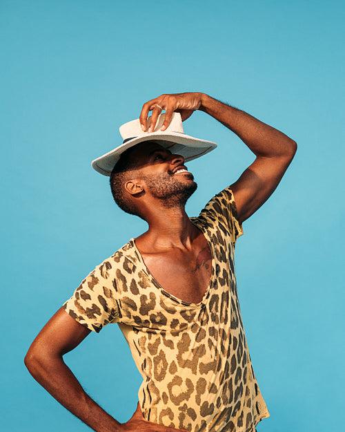 Cheerful guy in stylish clothes holding straw hat under his head in studio