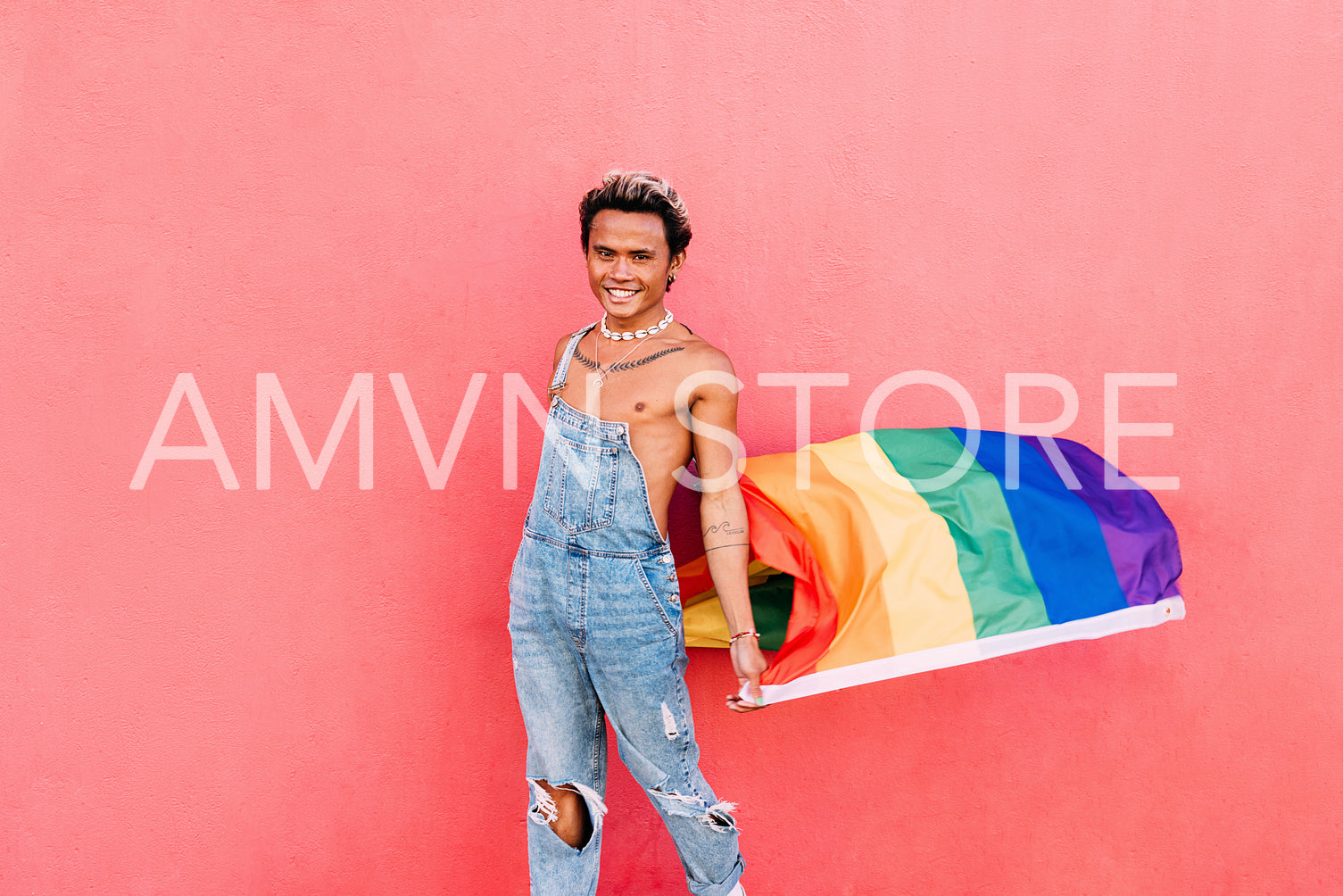 Happy male in denim casuals standing with LGBT flag at pink wall