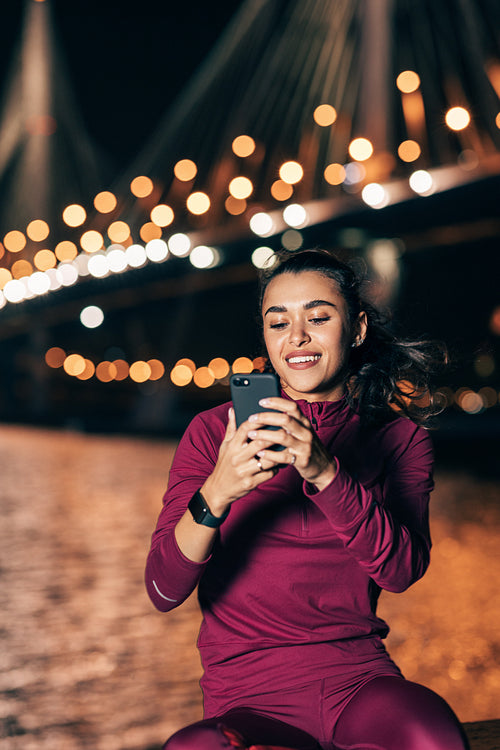 Smiling woman holding a smartphone while relaxing during training at night