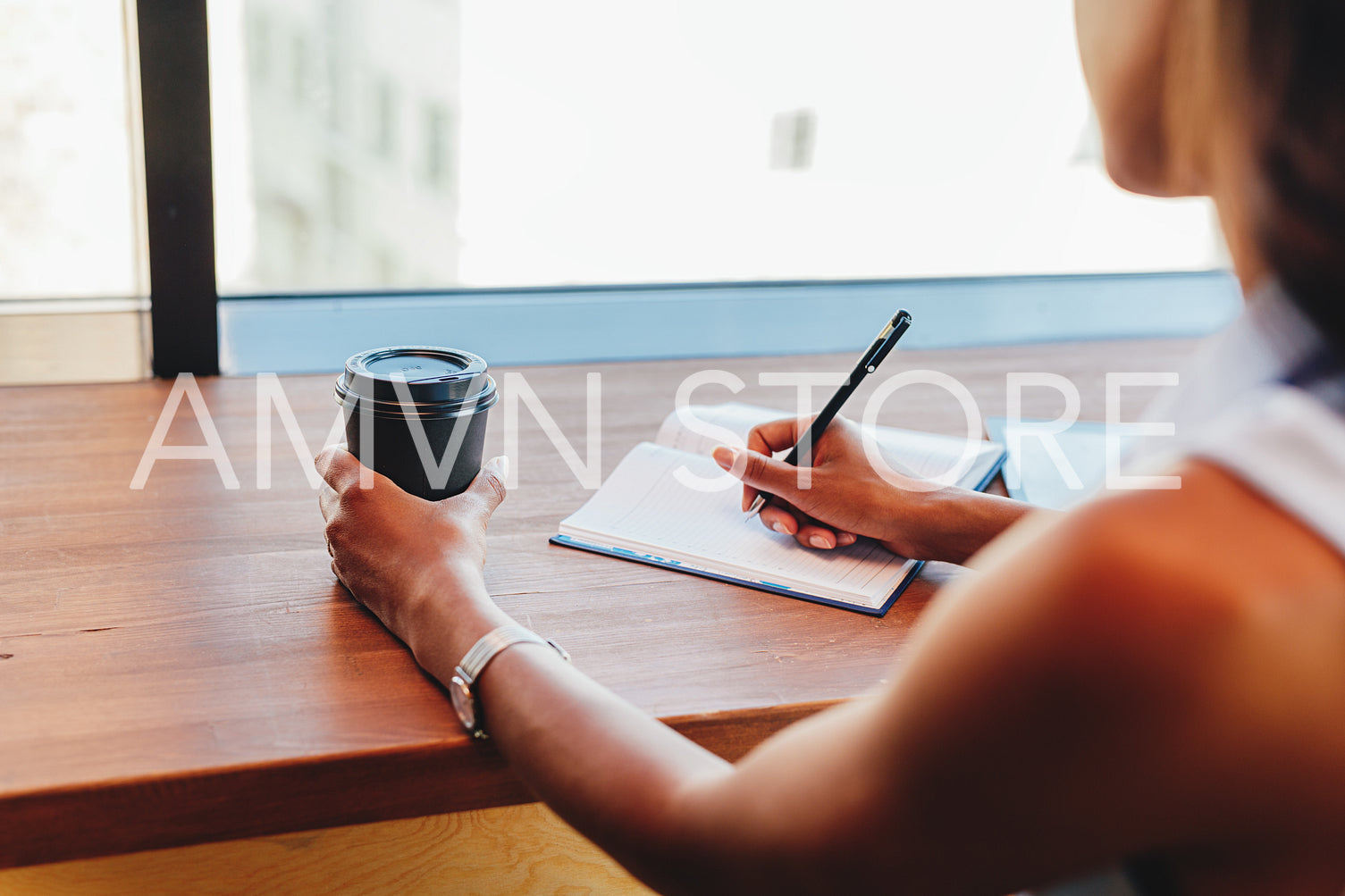 Unrecognizable freelance woman writing in notebook at cafe	